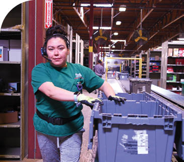 A woman in a green shirt is working in a factory, handling a large box. AI generated content